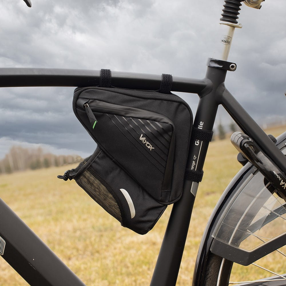 Czarna torba rowerowa przymocowana do czarnej ramy, zielone i białe akcenty, tło pola.