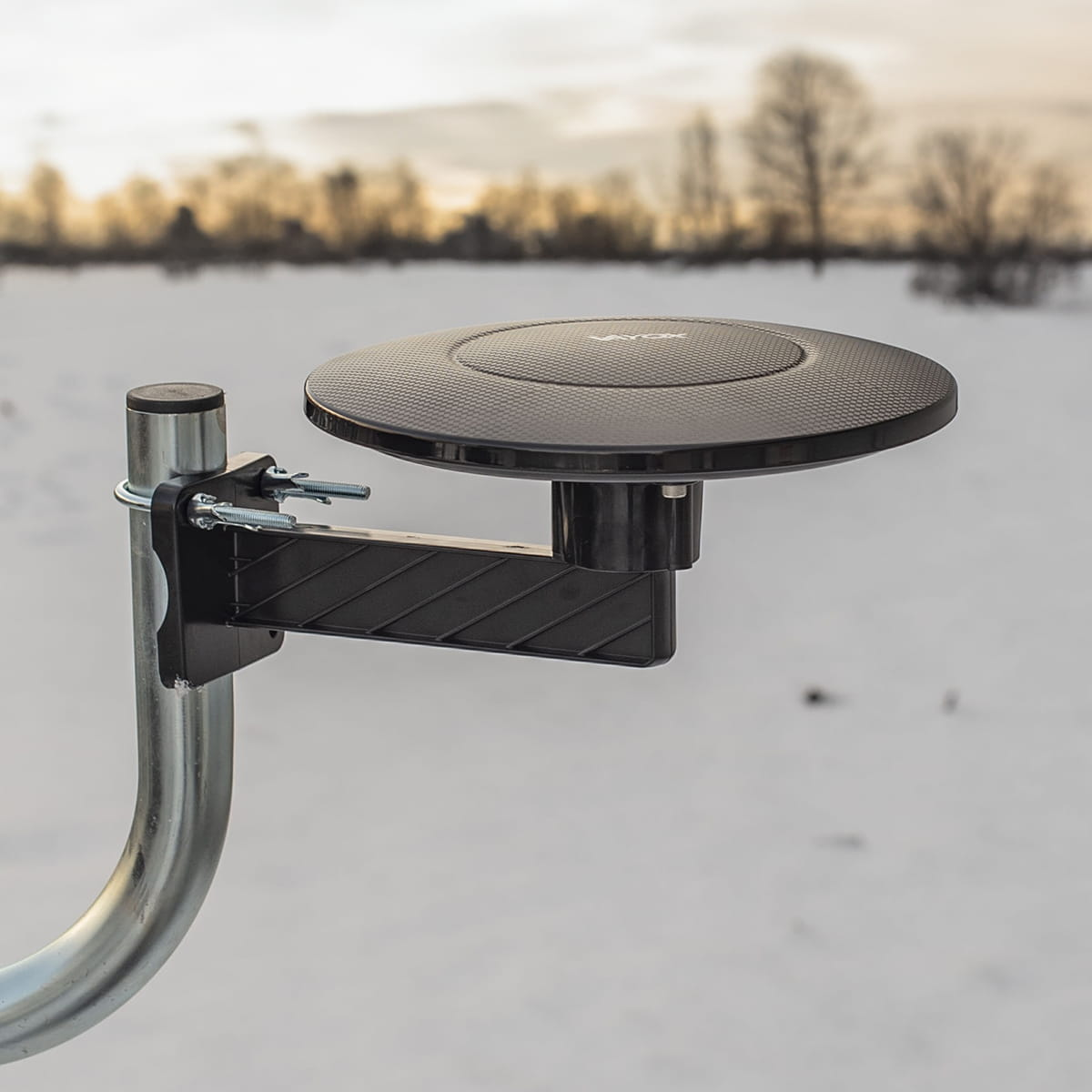 Czarna antena satelitarna na słupie, na zaśnieżonym polu.