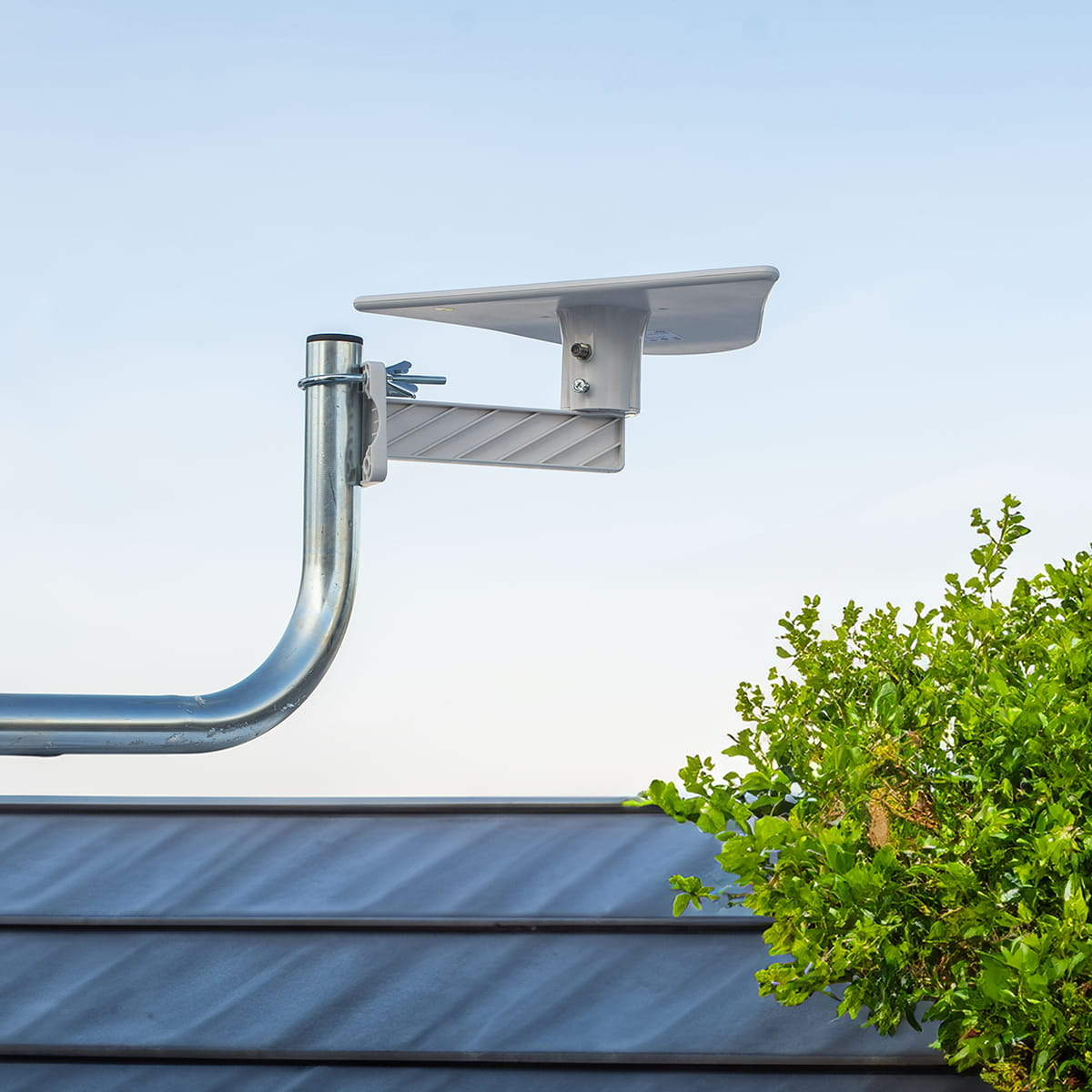 Srebrna antena na dachu, z zielenią w prawym dolnym rogu i błękitnym niebem.