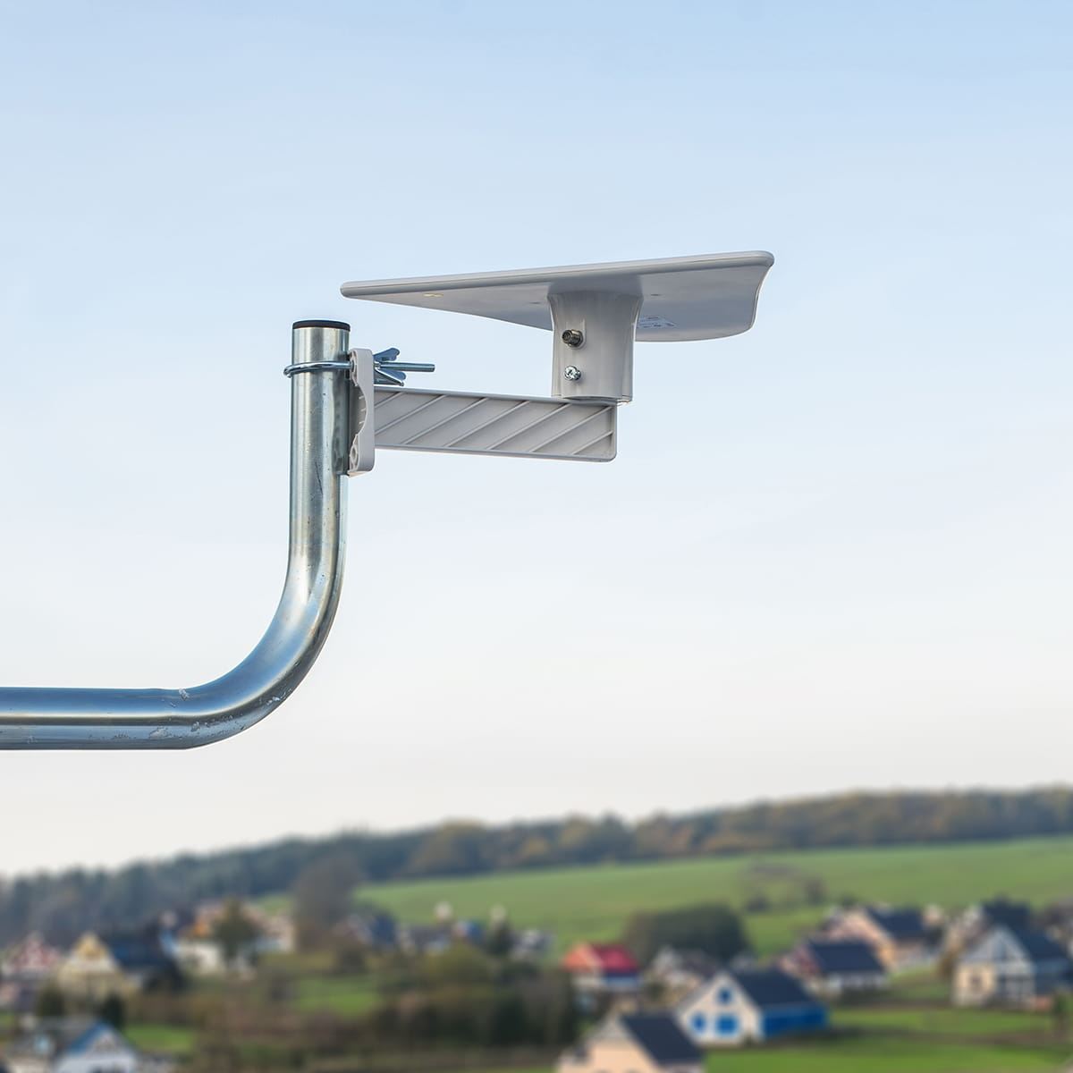 Srebrna antena na dachu, z rozmytym tłem domów i zielonych wzgórz.