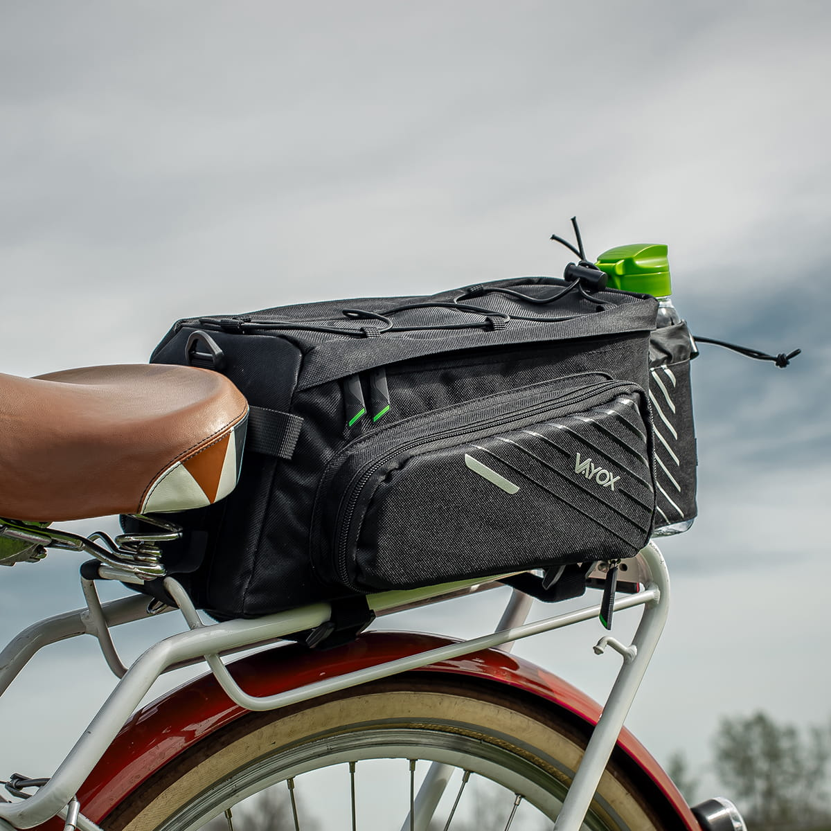 Czarna torba rowerowa z butelką wody, zamontowana na rowerze nad brązowym siodełkiem.