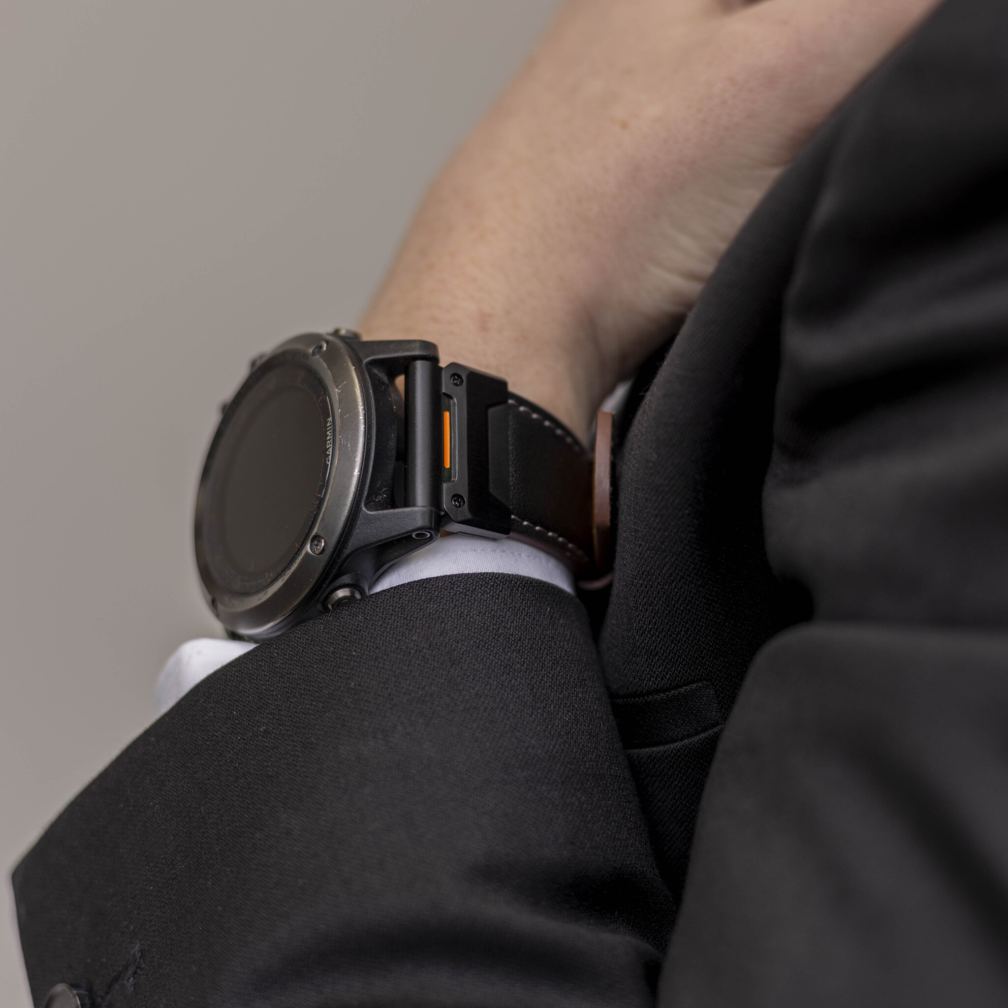 Das Handgelenk einer Person mit einer schwarzen Garmin-Uhr. Das Handgelenk befindet sich in einem Anzugärmel.