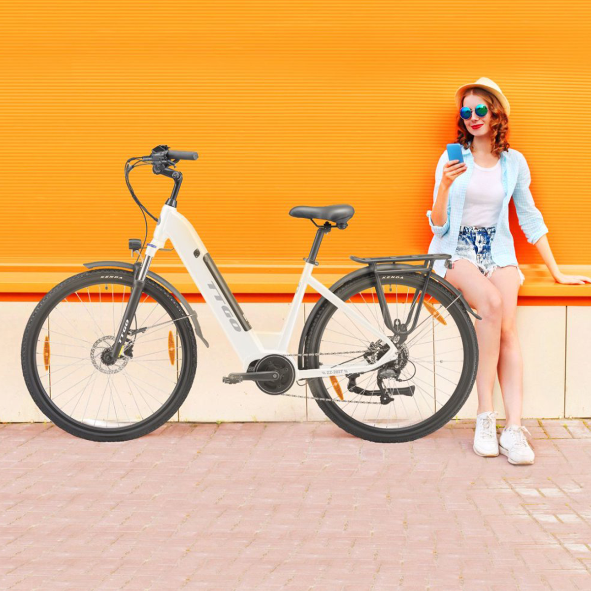 Kobieta z rowerem przy pomarańczowej ścianie, korzystająca z telefonu.