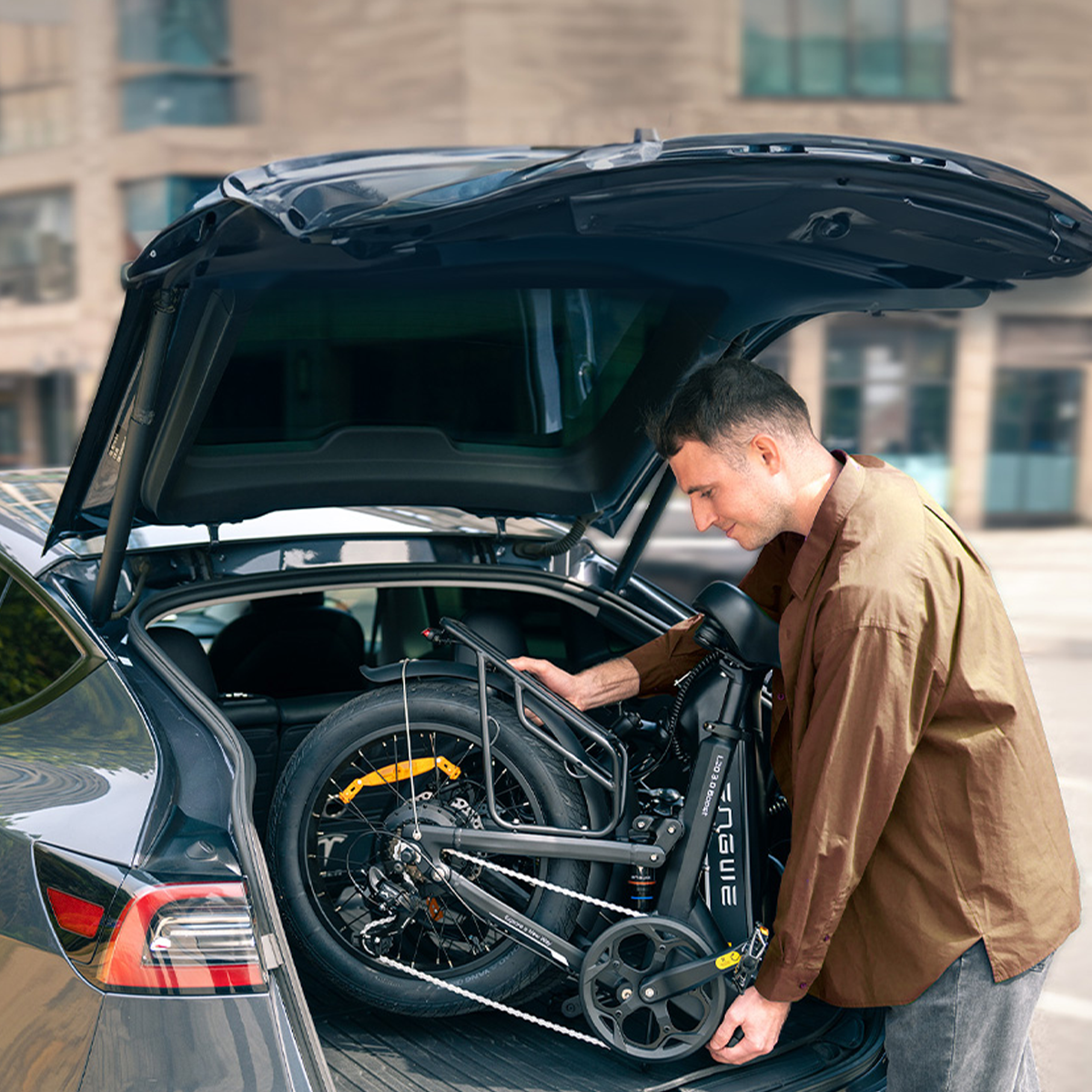 Mężczyzna ładuje rower elektryczny do bagażnika. Samochód i budynki w tle.