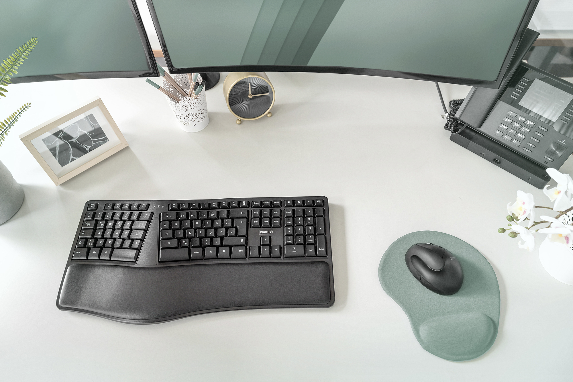 Una scrivania con tastiera nera, mouse e due monitor. C'è un orologio e decorazioni.
