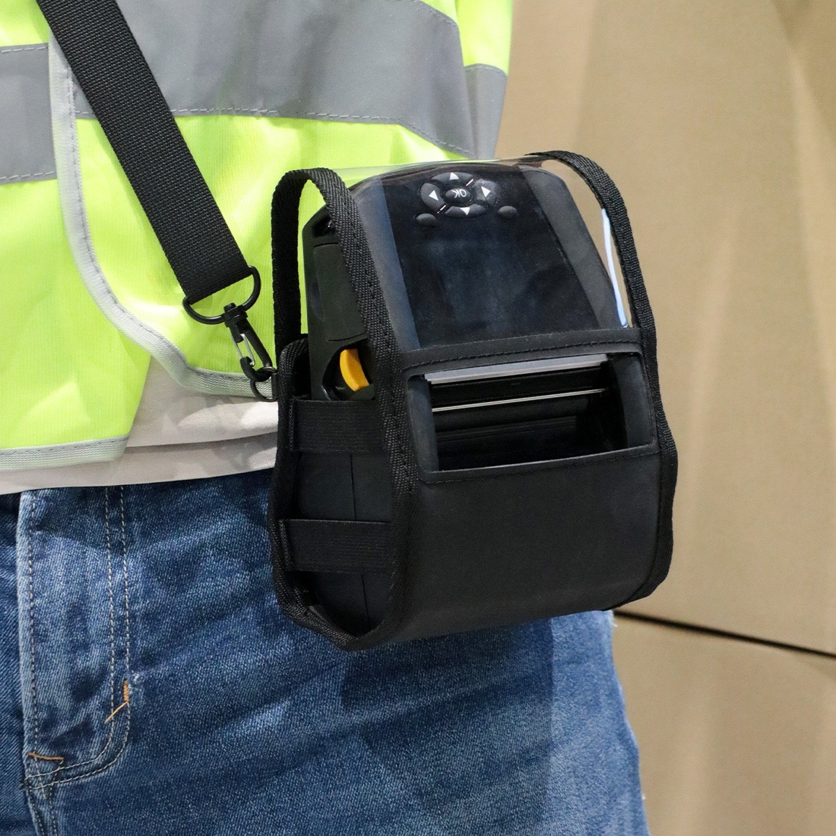 Czarna przenośna drukarka w etui, noszona na ciele osoby za pomocą paska. Osoba ma na sobie kamizelkę.