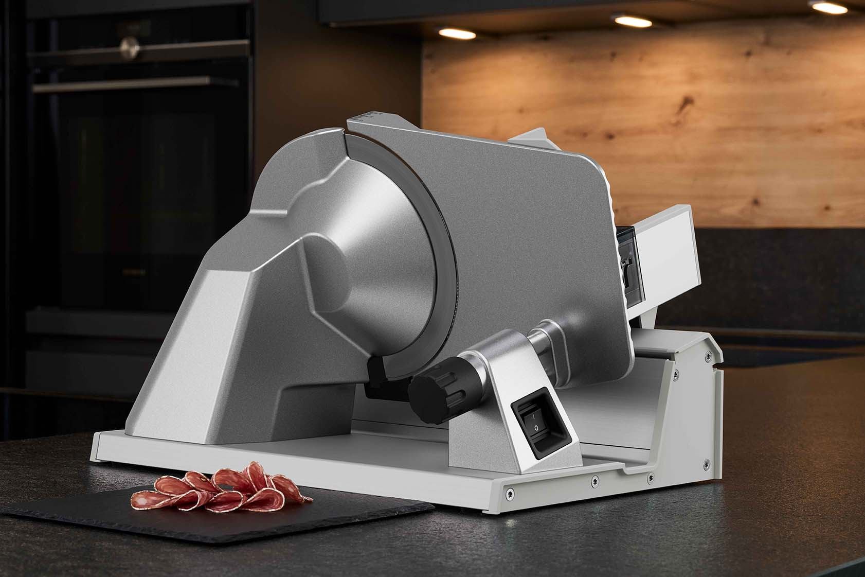 Srebrna krajalnica do mięsa z pokrojonym mięsem na czarnej desce. Kuchnia z drewnianym i ciemnym tłem.