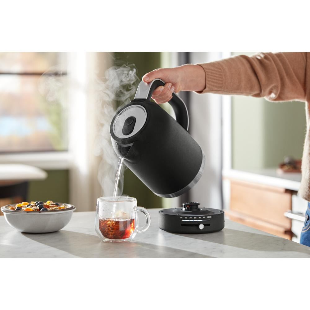 Person pouring water from a black kettle into a glass of tea.
