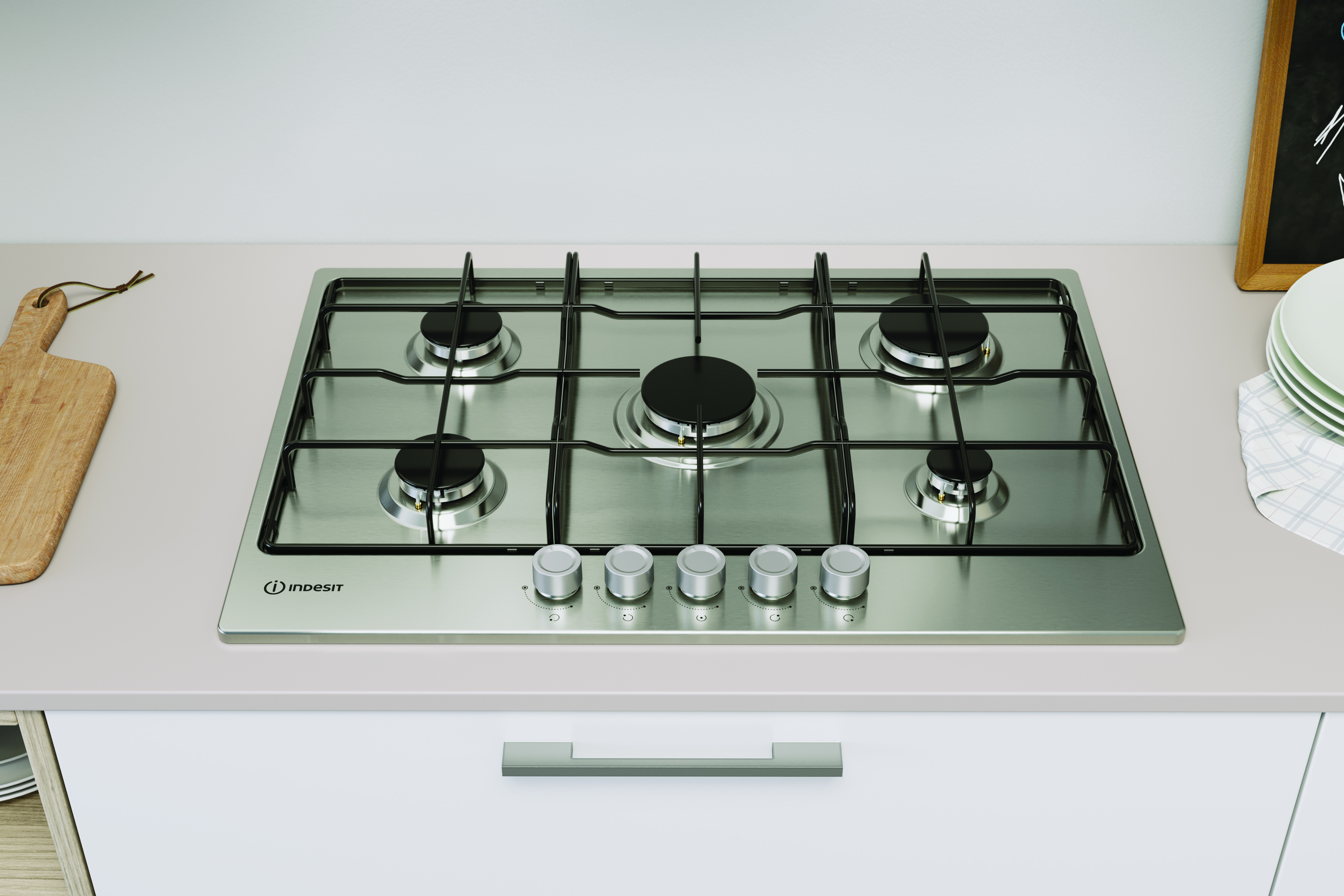Stalowa płyta gazowa z pięcioma palnikami na białej szafce, z logo Indesit.