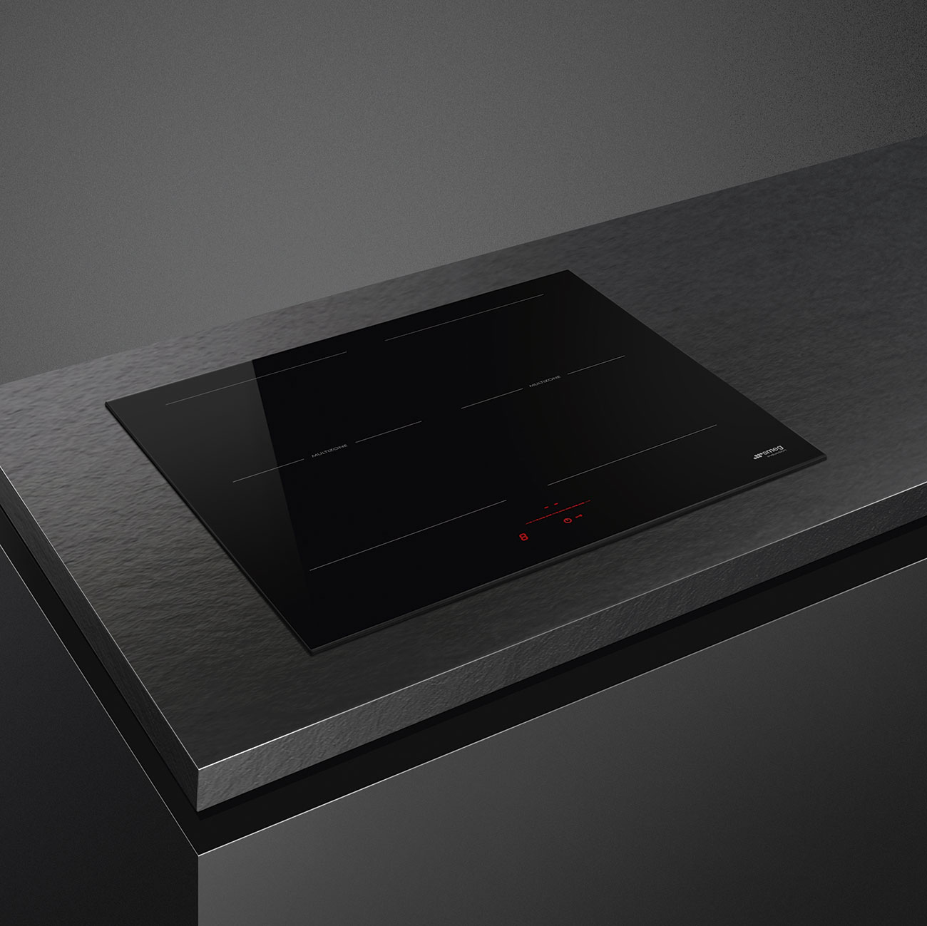 Piano cottura nero con display digitale. Logo Smeg in basso a destra. In un ambiente cucina scuro.