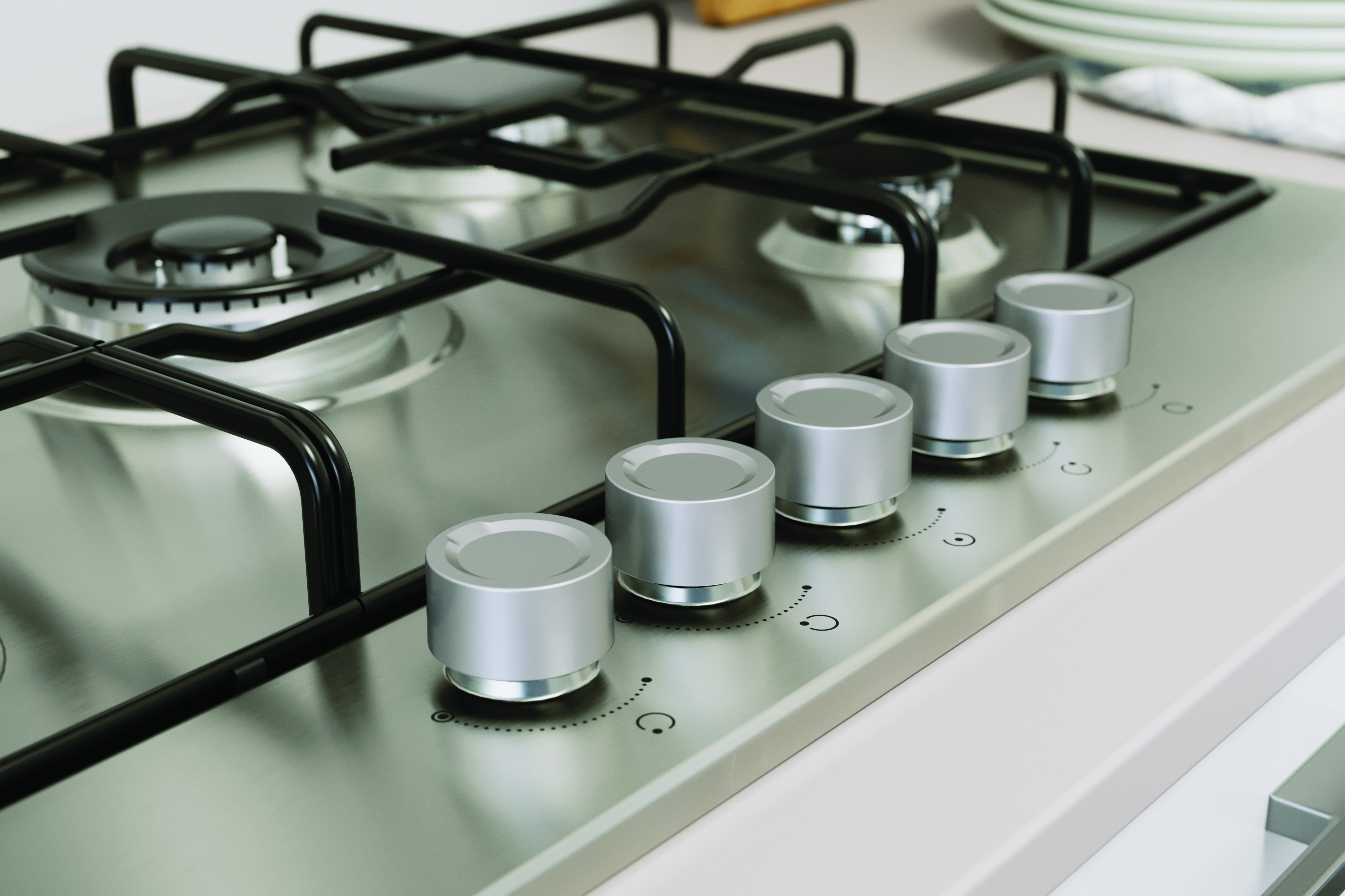 Zbliżenie na pokrętła sterowania płyty ze stali nierdzewnej. Widoczne srebrne pokrętła ze znacznikami ustawień ciepła.
