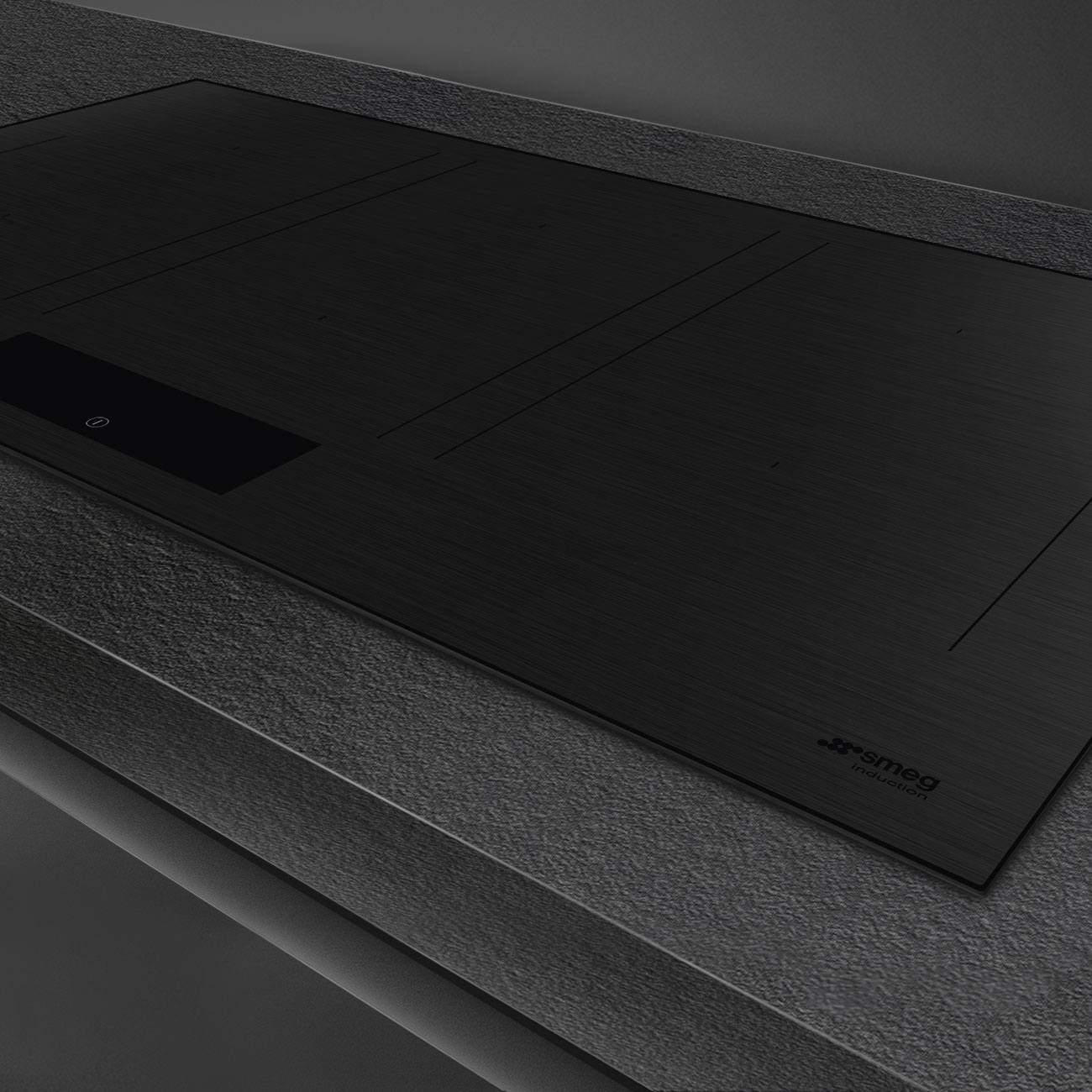 Un piano cottura a induzione nero con pannello a sfioramento e logo Smeg, su un piano di lavoro grigio scuro.