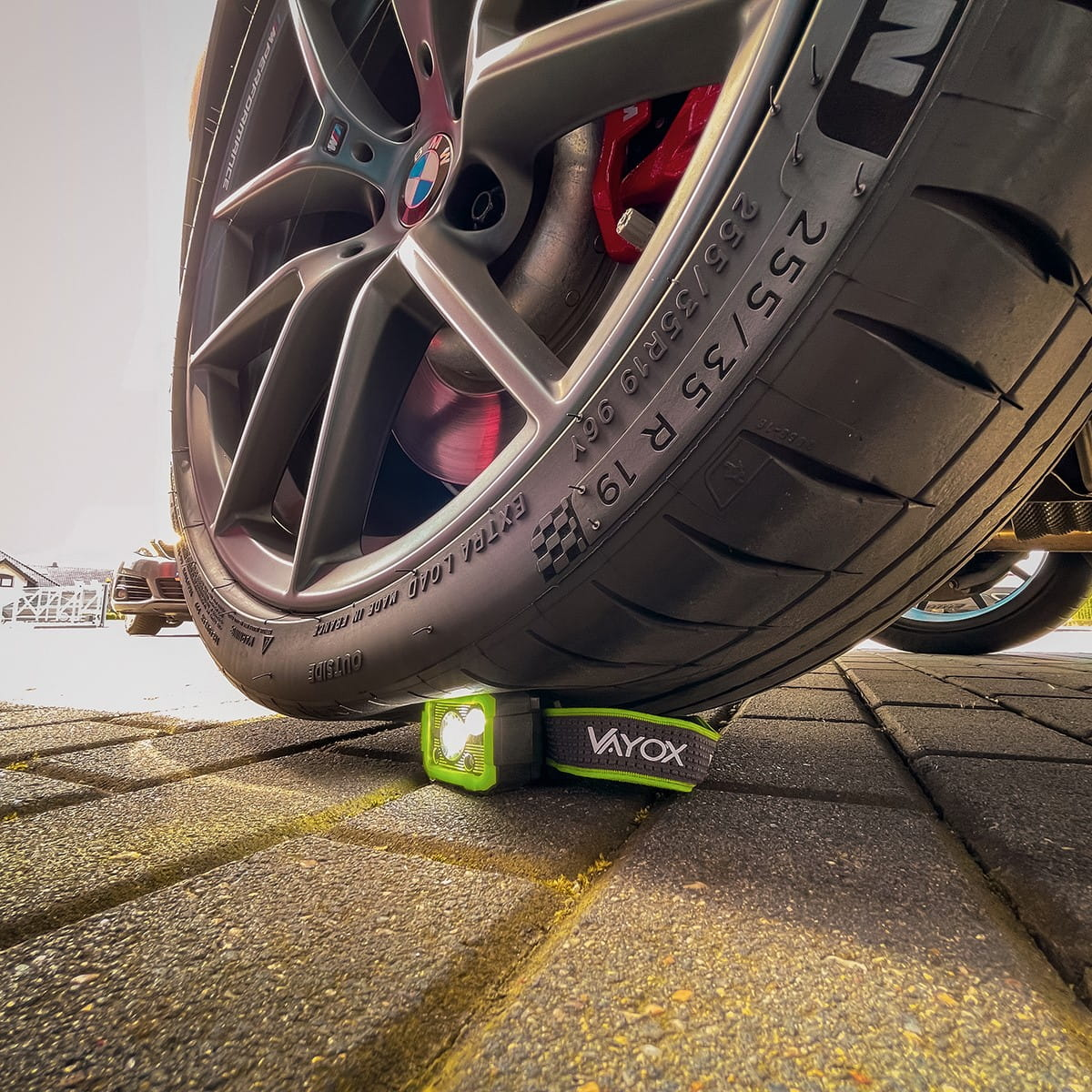 Zielono-czarna latarka czołowa znajduje się pod oponą samochodu na ceglanej drodze.