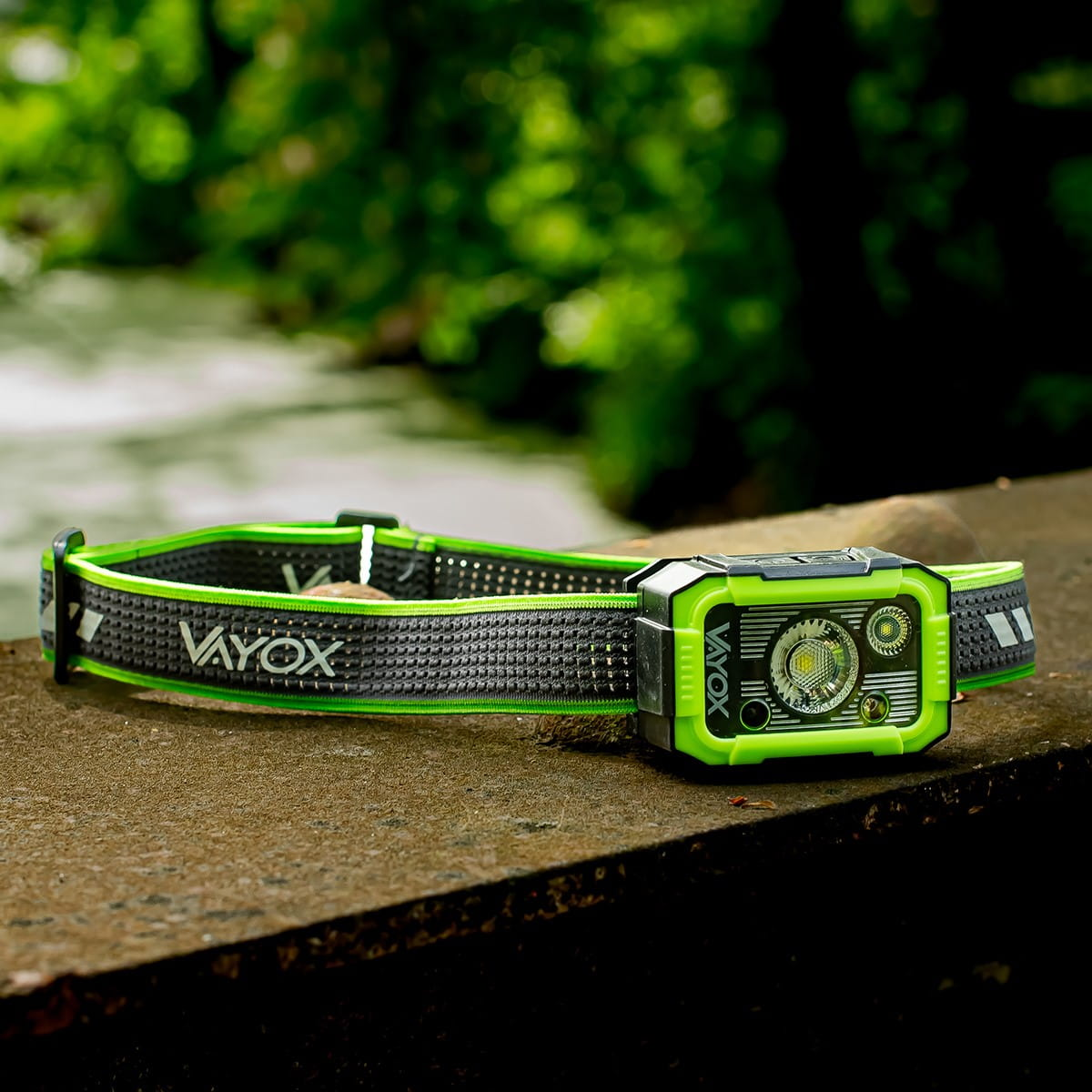 Latarka czołowa na kamiennej ścianie. Latarka czołowa jest czarna i ma zielony akcent.