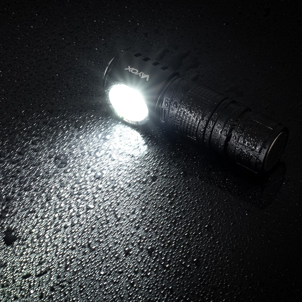 Czarna latarka czołowa świeci jasnym światłem na mokrej, ciemnej powierzchni z kroplami wody.