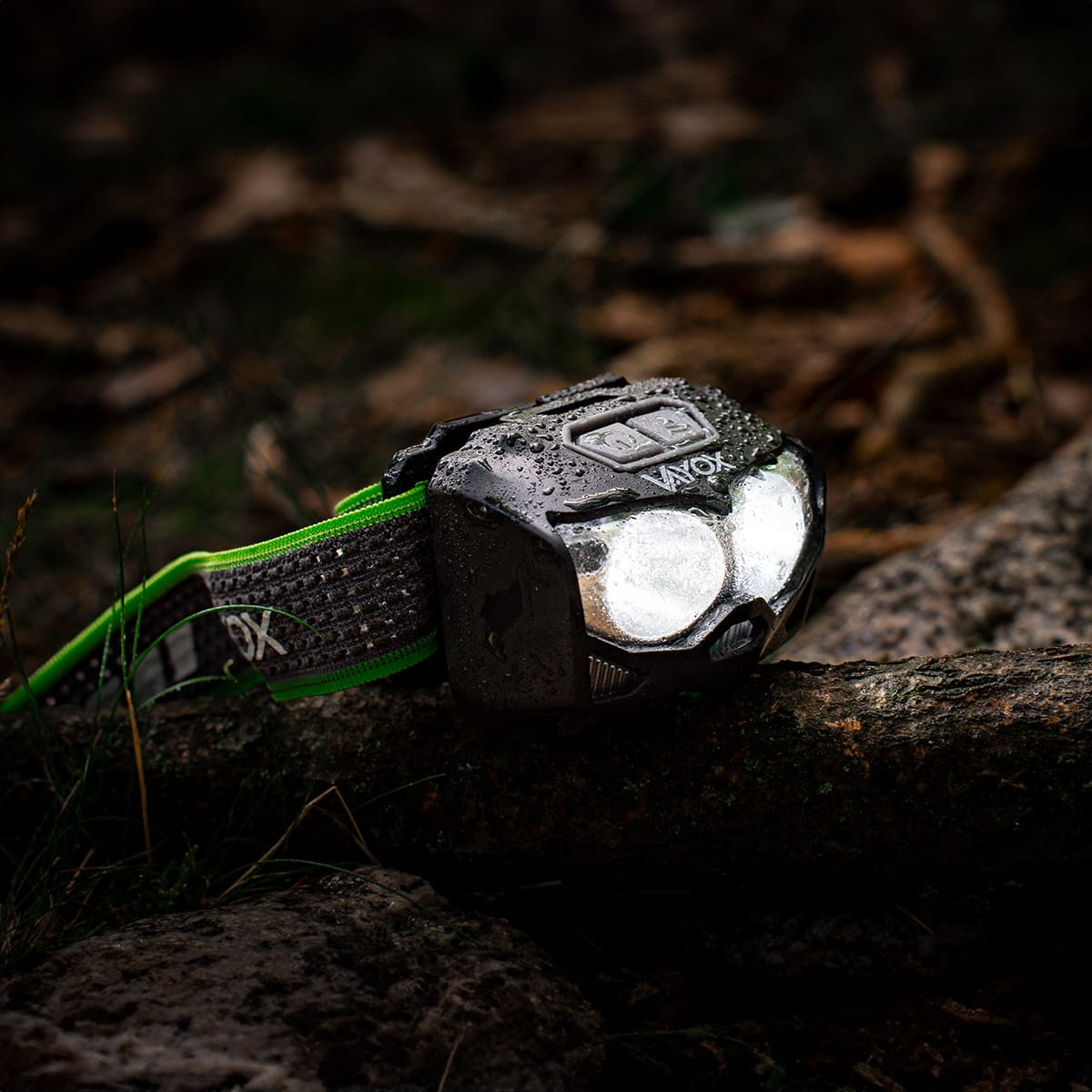 Czarna latarka czołowa z marką VAYOX na pniu. Latarka jest włączona.