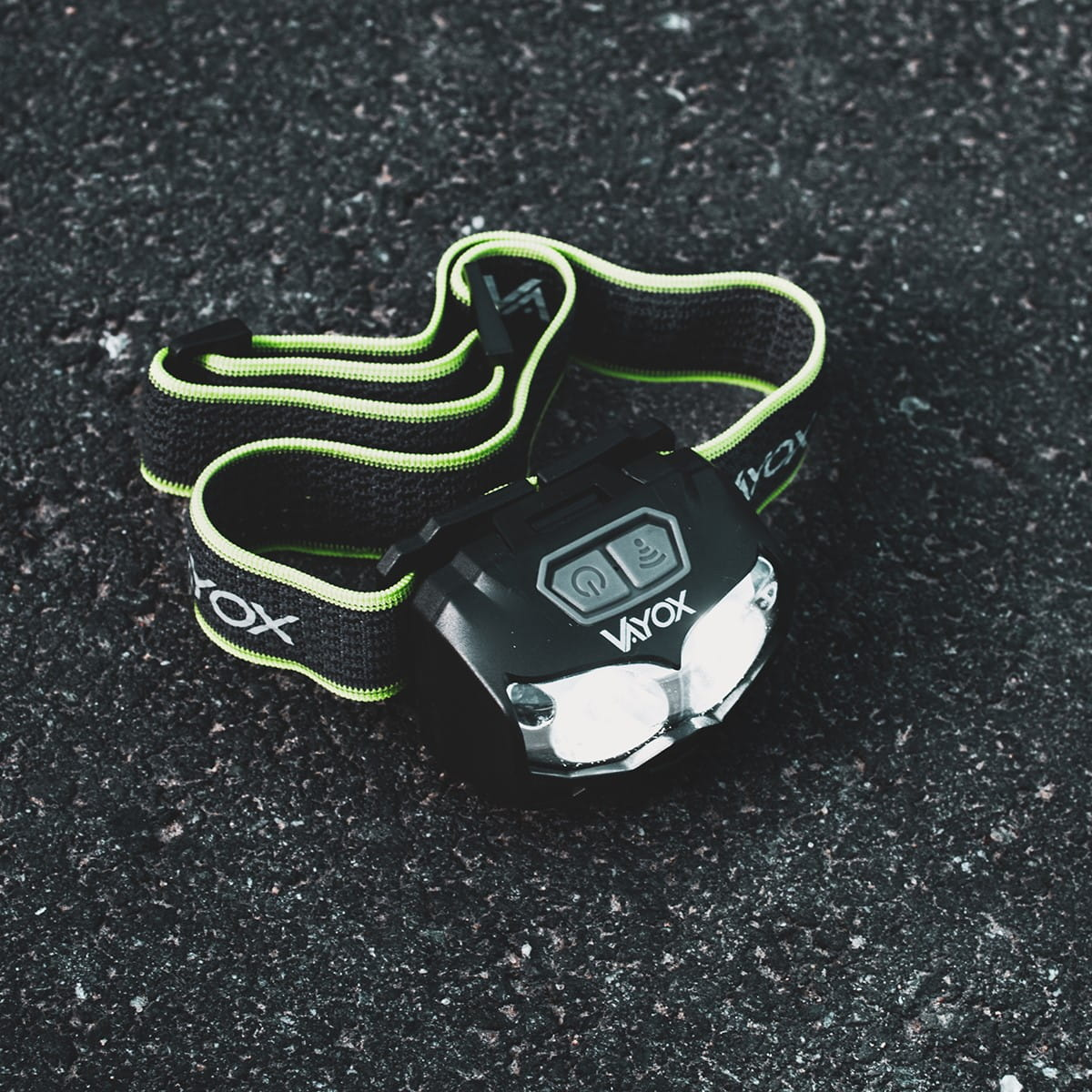 Czarna latarka czołowa z marką VAYOX na ciemnej powierzchni. Latarka jest włączona.