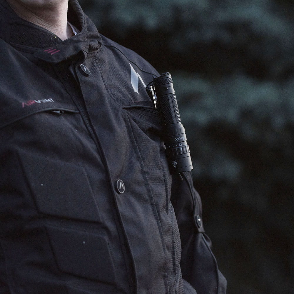 Osoba w kurtce z latarką w kieszeni. Latarka jest czarna i cylindryczna.