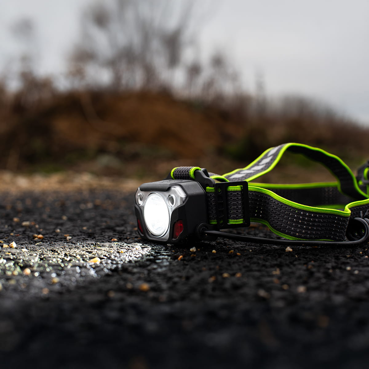 Latarka czołowa na asfalcie. Światło jest włączone, oświetla ziemię. Tło jest rozmyte.