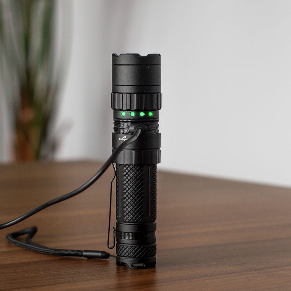 Czarna latarka ładująca się na drewnianym stole. Świecą się zielone światła.