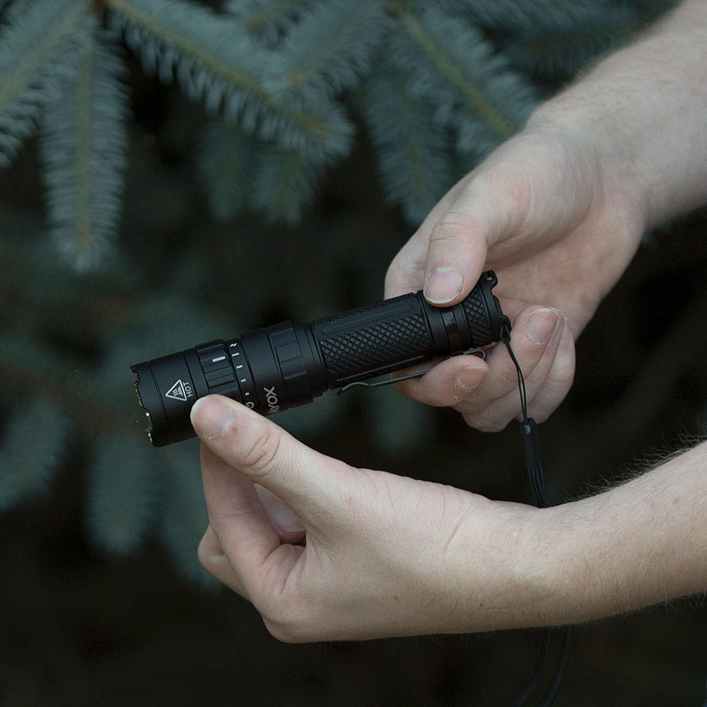 Osoba trzymająca czarną latarkę z radełkowanym uchwytem.