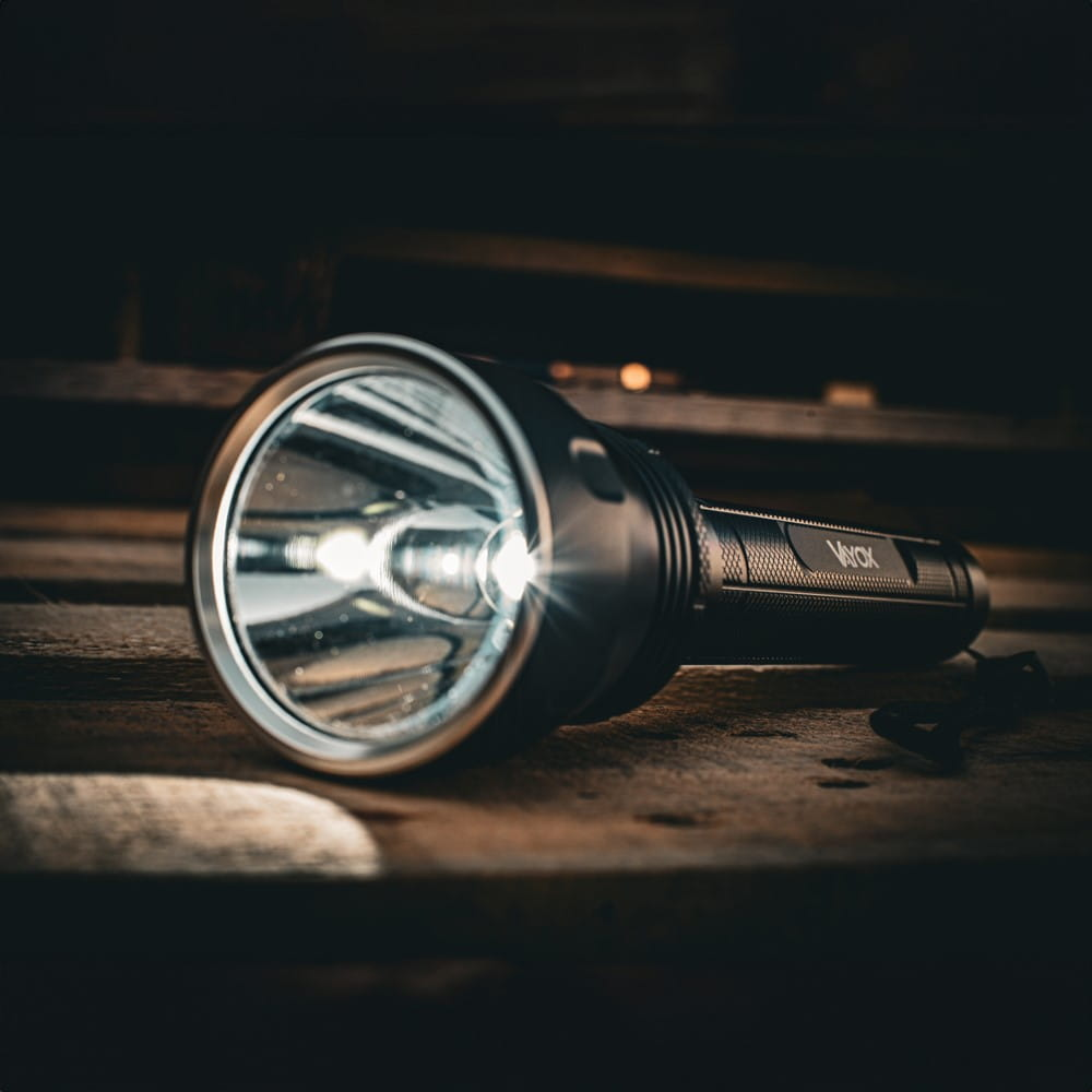 Czarna latarka z jasnym strumieniem światła na drewnianej powierzchni.