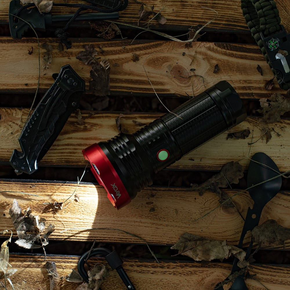 Latarka spoczywa na drewnianych deskach. Nóż, łyżka i inne narzędzia obok.