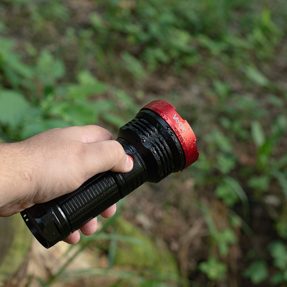 Ręka trzymająca czarną latarkę z czerwoną ramką w naturze.