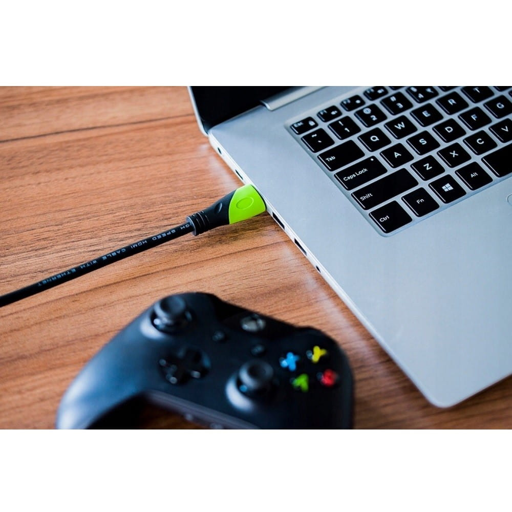 Laptop z wpiętym kablem HDMI i czarnym kontrolerem do gier wideo.