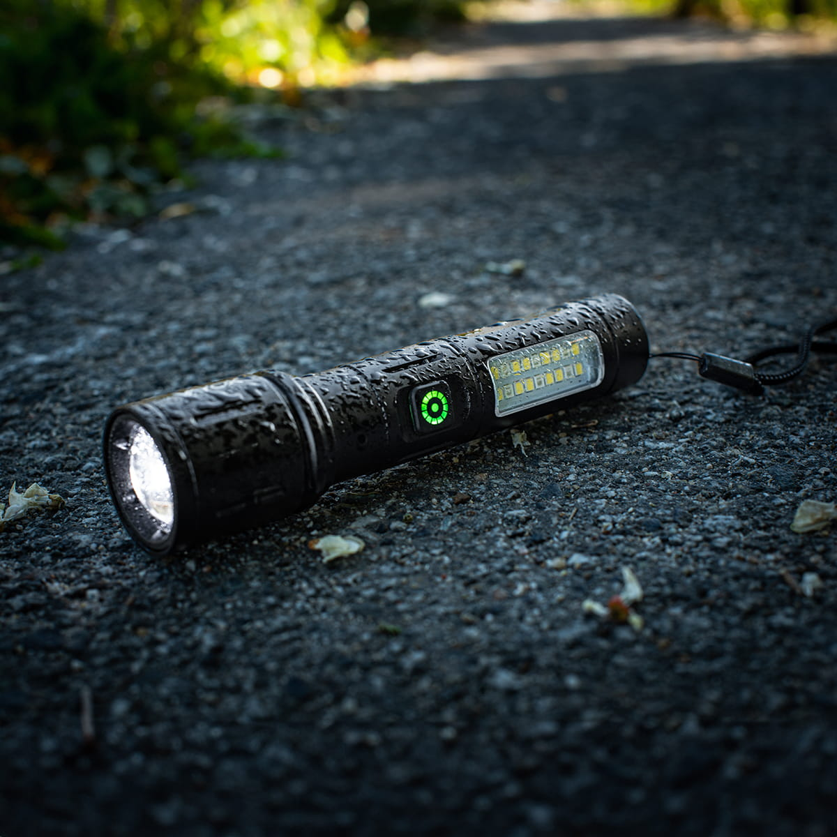 Czarna latarka Vayox na żwirowej ścieżce. Pokazuje świecące światło.