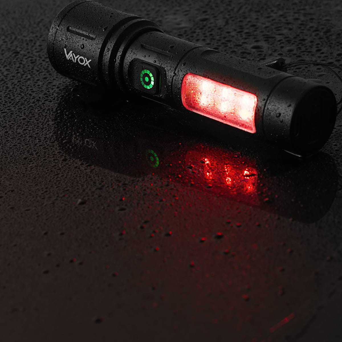 Czarna latarka Vayox na mokrej powierzchni. Pokazuje czerwone światło.