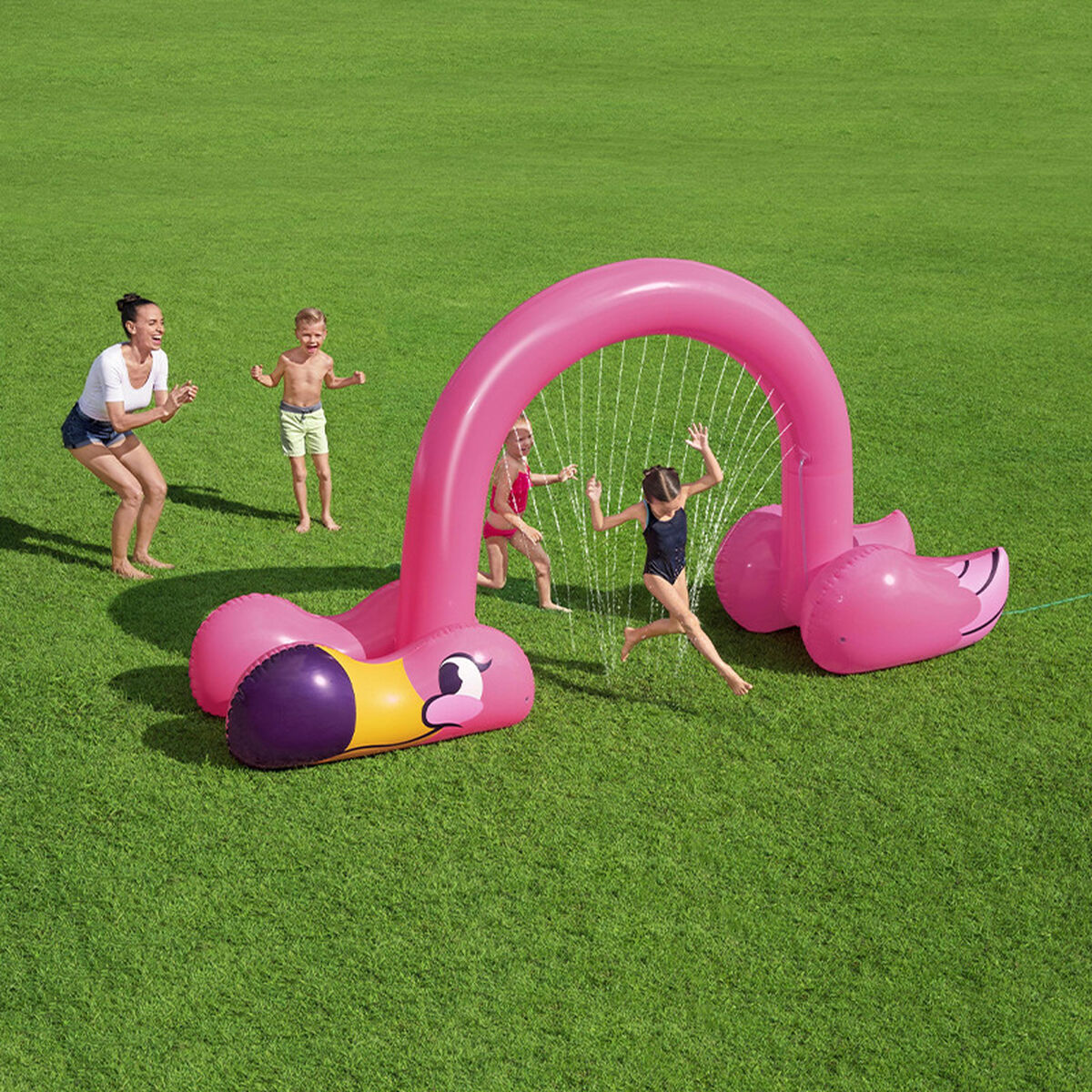 Niños jugando bajo un arco de aspersor de flamenco rosa en un césped verde.