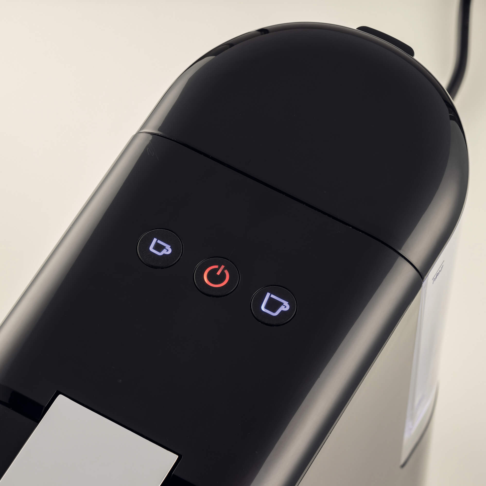 Zbliżenie czarnego ekspresu do kawy z podświetlanymi przyciskami: kawa, zasilanie i kawa.