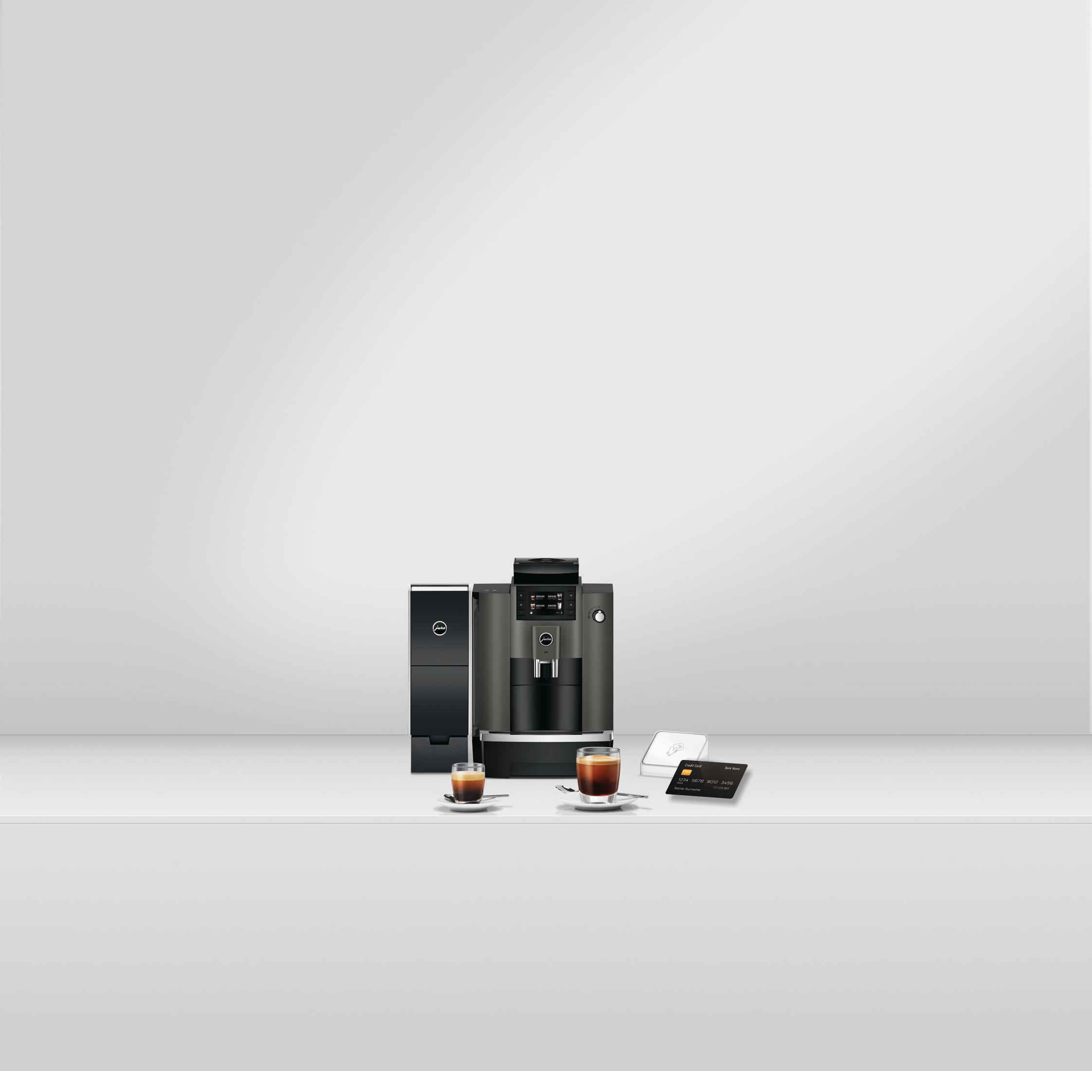 Ekspres do kawy z dwiema filiżankami kawy na białym stole. Czarny stojak z boku.