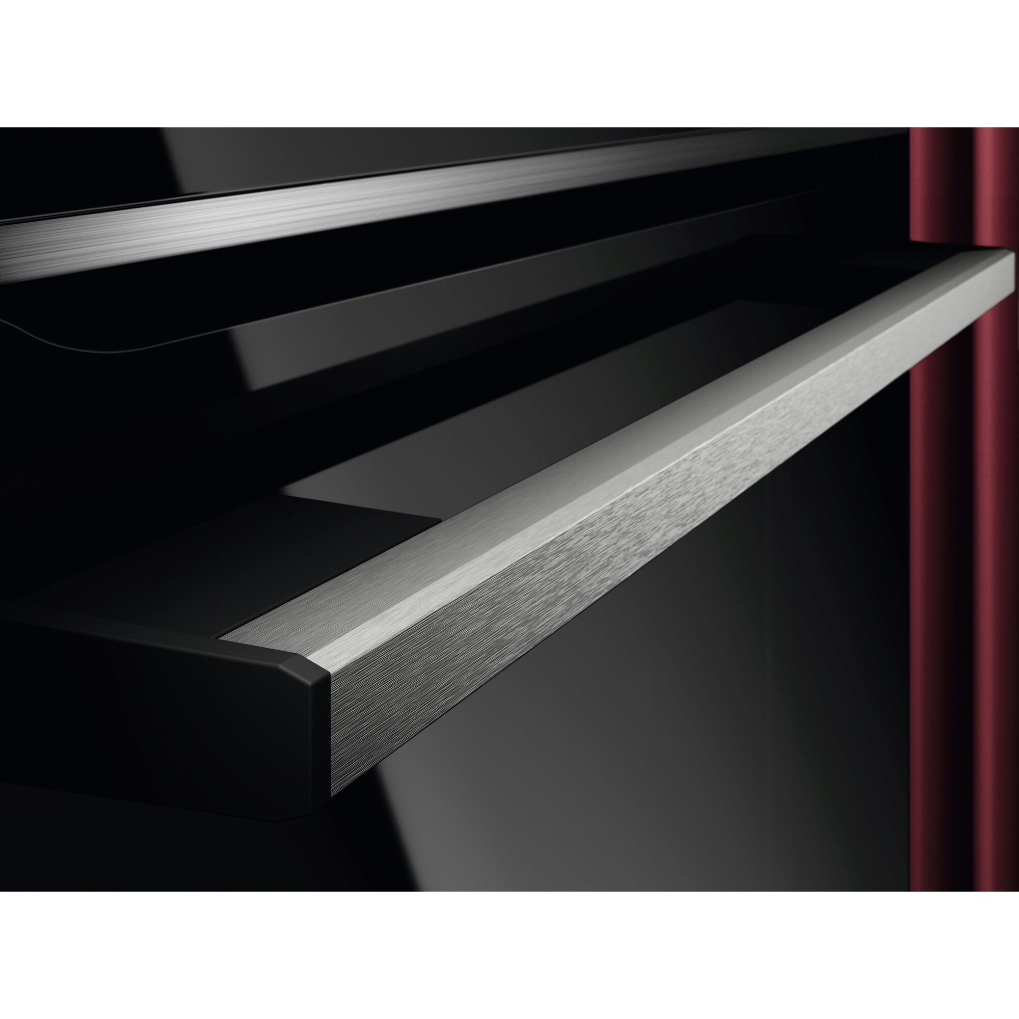 Zbliżenie szuflady z metalowym uchwytem. Szuflada jest w czarnym piekarniku z czerwoną ścianą.