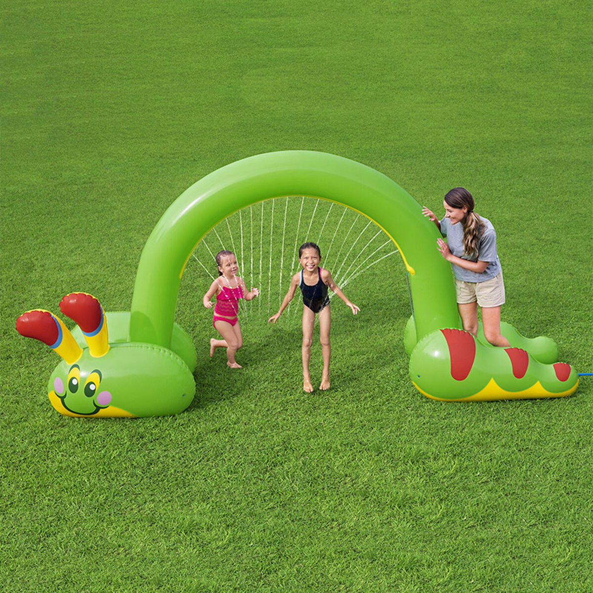 Niños jugando en un aspersor de agua con forma de oruga verde.