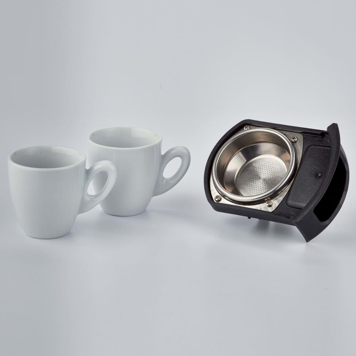 Dwa białe kubki i czarny kolbowy z filtrem. Wszystko na białej powierzchni.