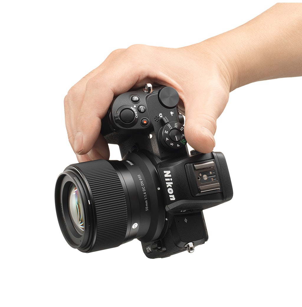 Osoba trzymająca aparat z obiektywem na białym tle; widoczny napis Nikon.