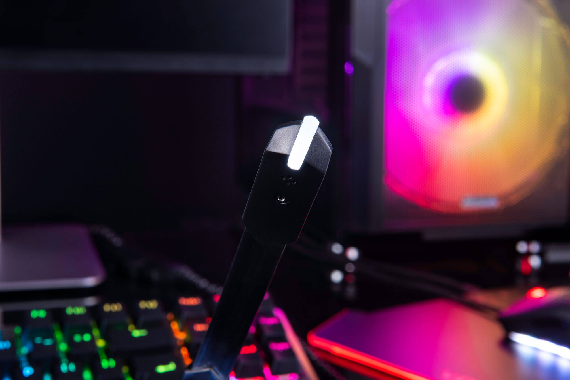 Czarny zestaw słuchawkowy dla graczy z mikrofonem. Klawiatura z kolorowymi światłami, PC w tle.