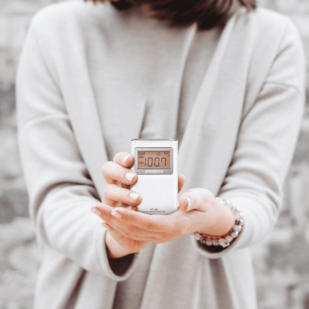 Kobieta trzymająca małe radio cyfrowe z wyświetlaczem pokazującym cyfry, w jasnym otoczeniu.