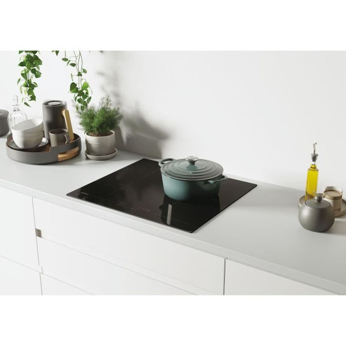 Blat kuchenny z płytą grzejną i garnkiem, kilka elementów dekoracyjnych i roślina.