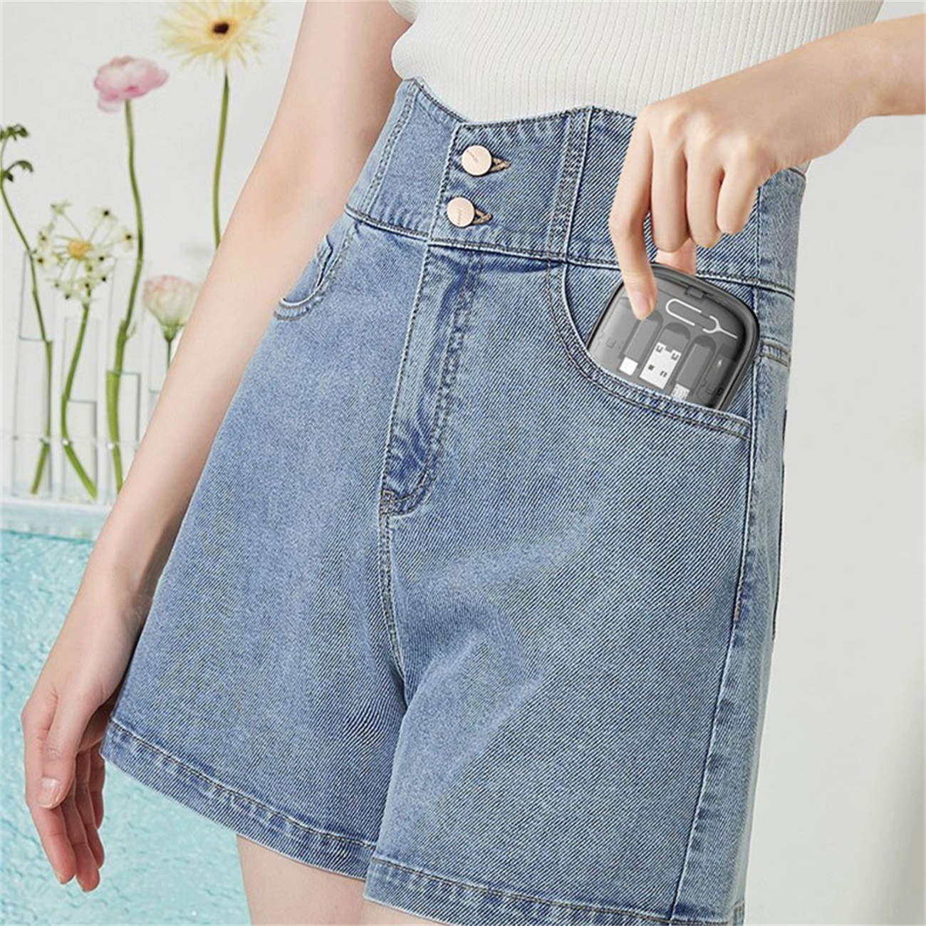 Die Hand einer Frau ist in einer Jeans-Shorts-Tasche. Ein kleiner Koffer ist sichtbar. High-Waist-Shorts.