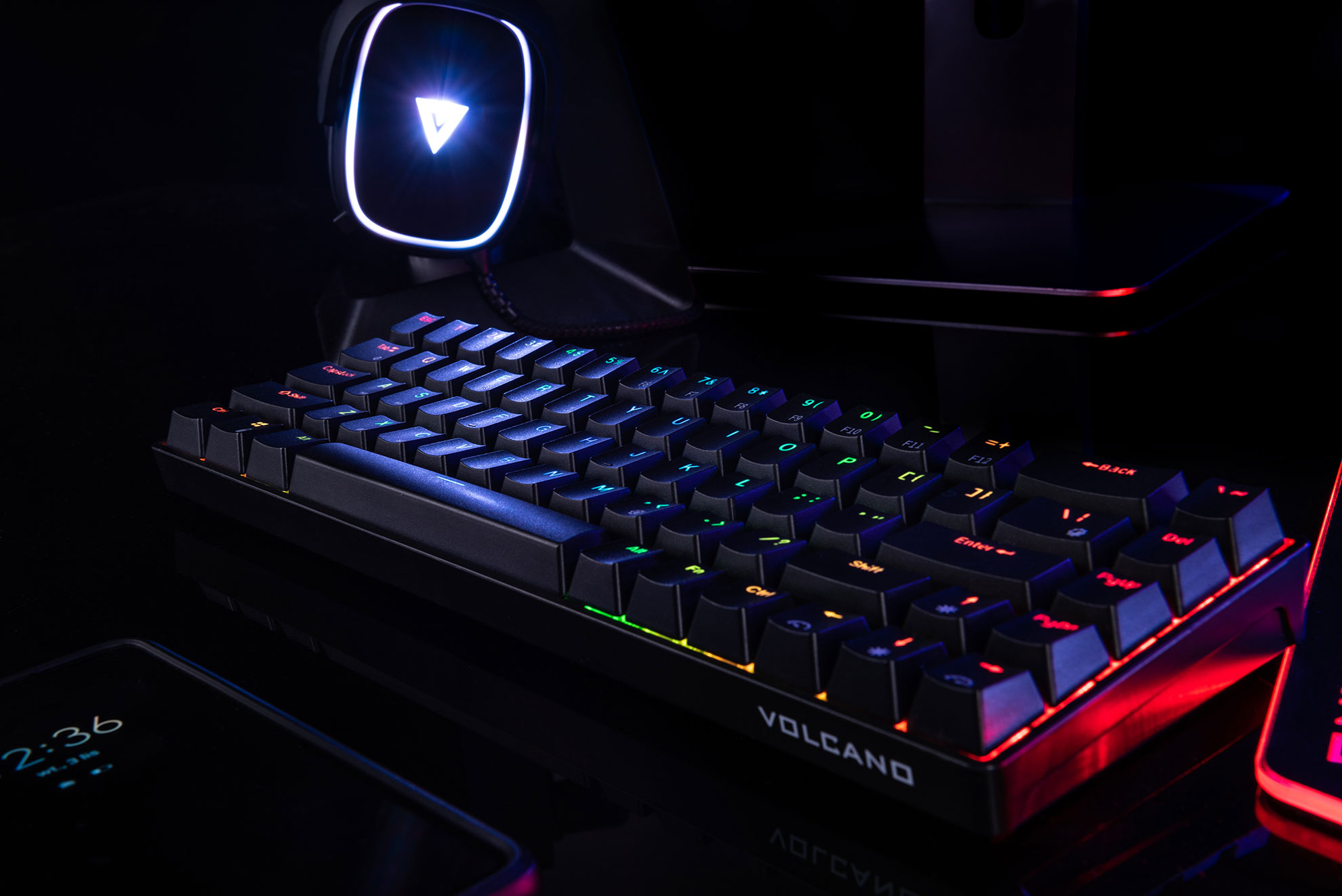Czarna klawiatura z tęczowym podświetleniem na ciemnej powierzchni, oświetlona przez monitor.