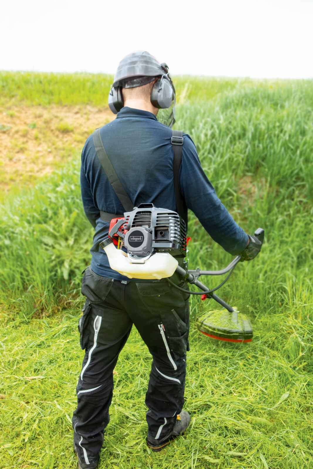 Hombre en campo usando recortadora. Lleva equipo de protección.