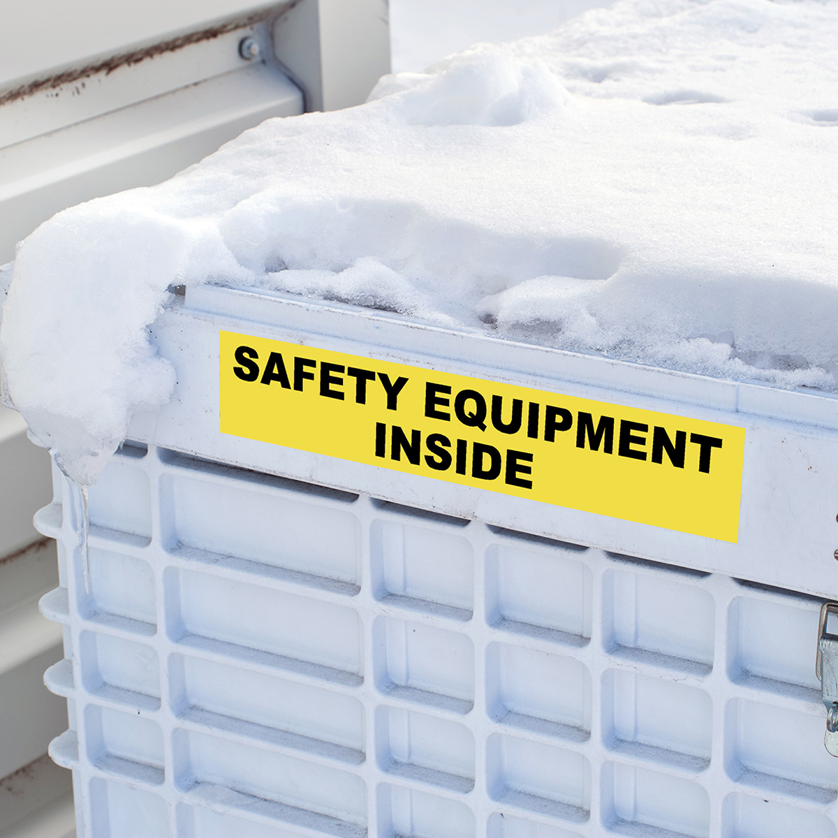 Żółta etykieta z napisem 'SAFETY EQUIPMENT INSIDE' na białym pojemniku ze śniegiem.