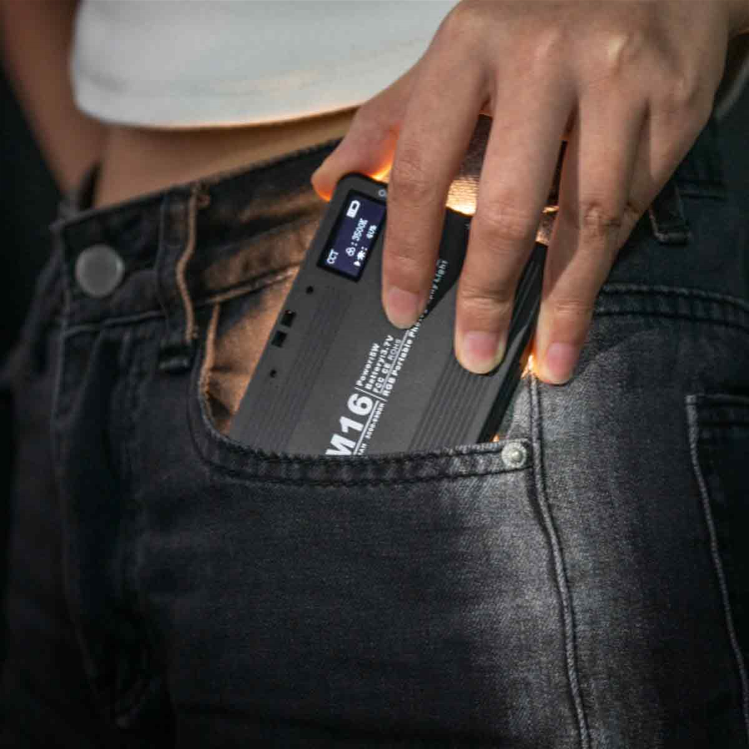 Die Hand einer Person, die ein kleines, schwarzes, rechteckiges Gerät in eine Jeans-Tasche steckt.