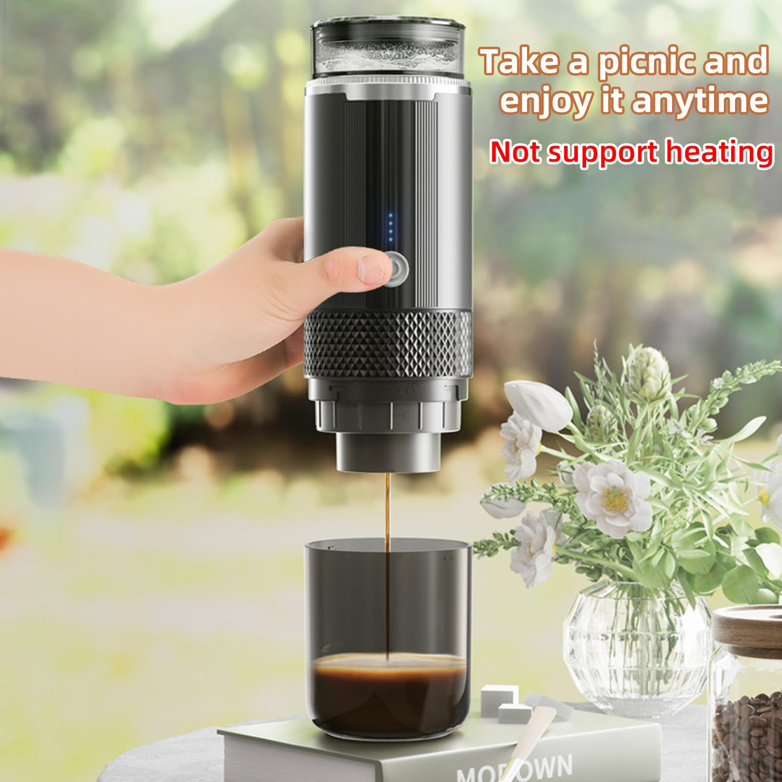 Eine Person gießt Kaffee aus einem tragbaren Kaffeezubereiter in eine Tasse, in der Nähe von Blumen und einem Buch.