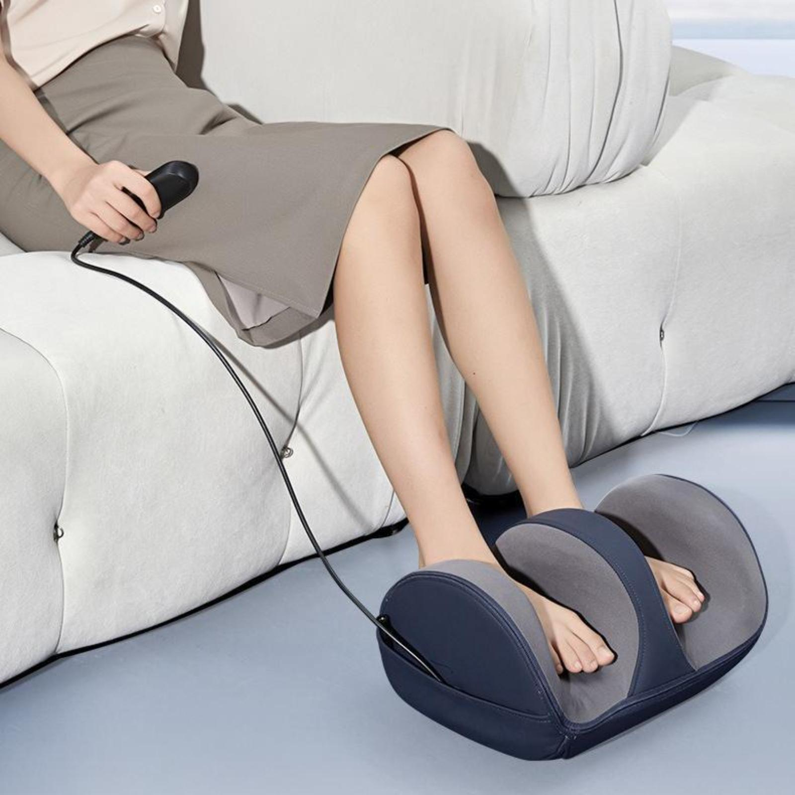 Eine Frau benutzt ein Fußmassagegerät, während sie auf einer Couch sitzt. Ihre Füße sind auf dem Massagegerät.