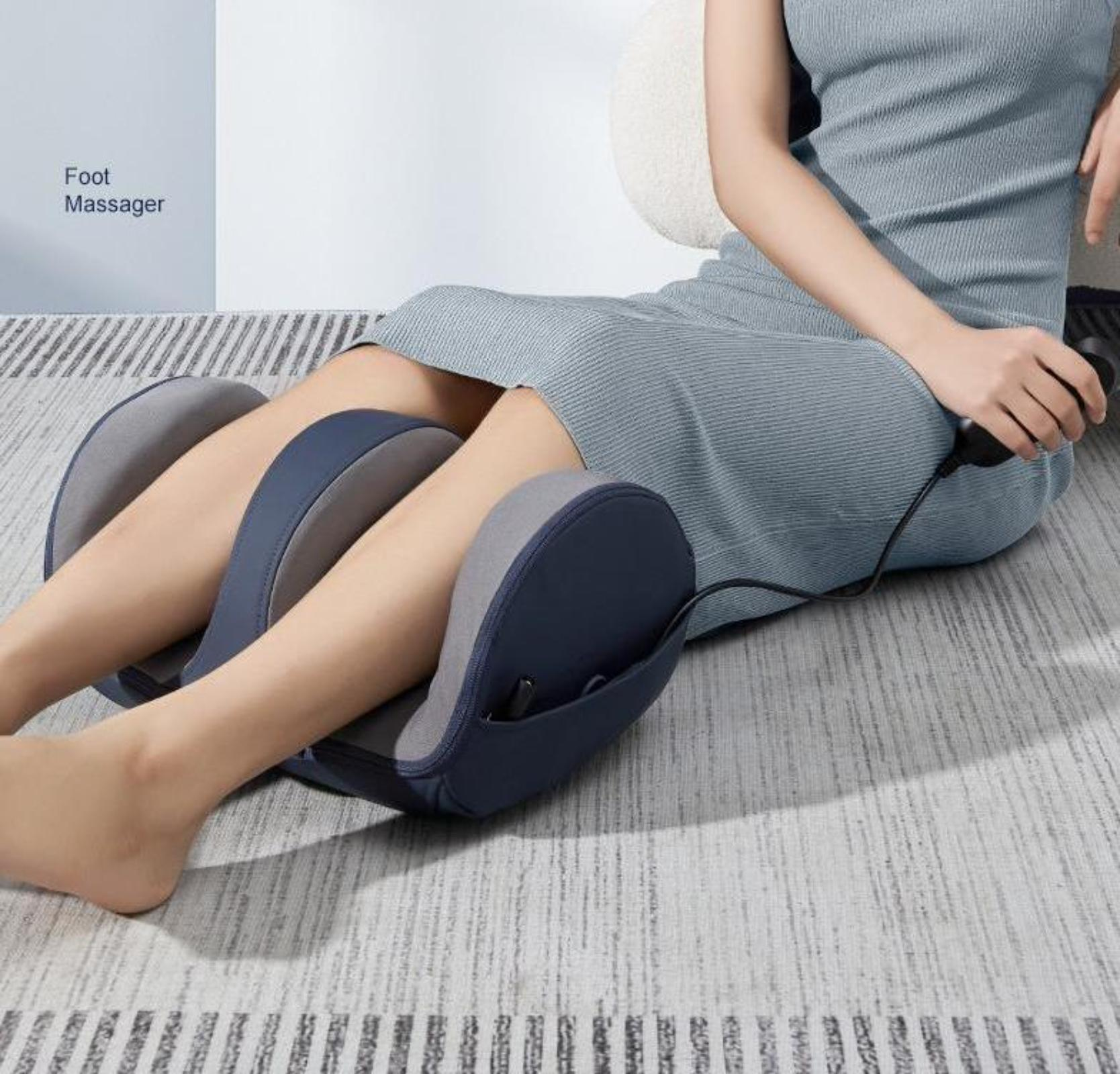 Eine Person sitzt auf einem Fußmassagegerät, die Beine darin. Der Hintergrund ist ein Raum.