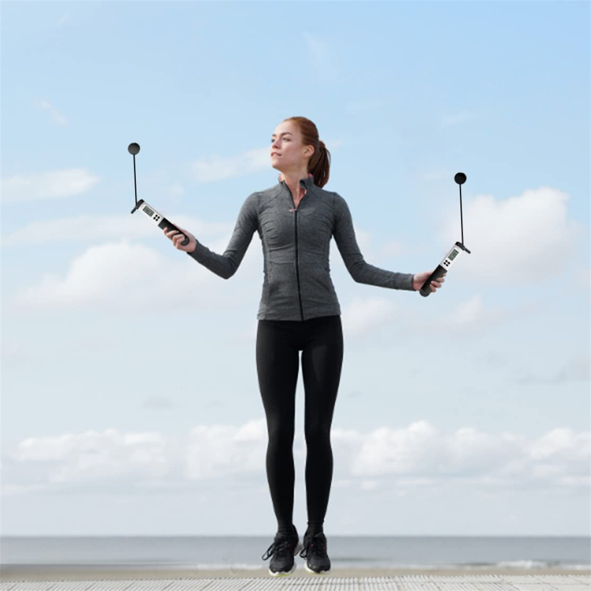 Frau, die mit zwei digitalen Springseilen springt, Himmel und Meer im Hintergrund.